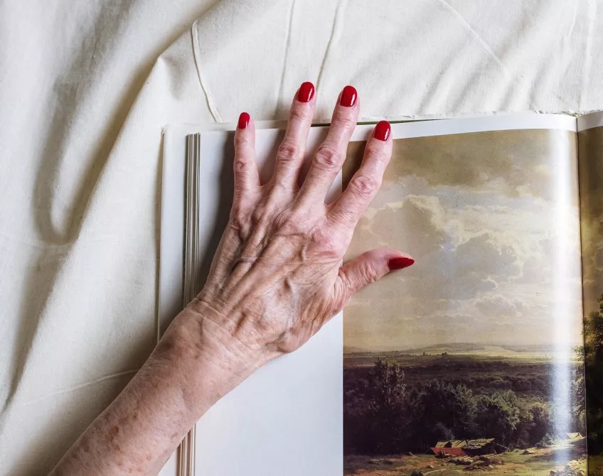 A photo of a hand with reumatism with red painted nails positioned on top of a photography book.